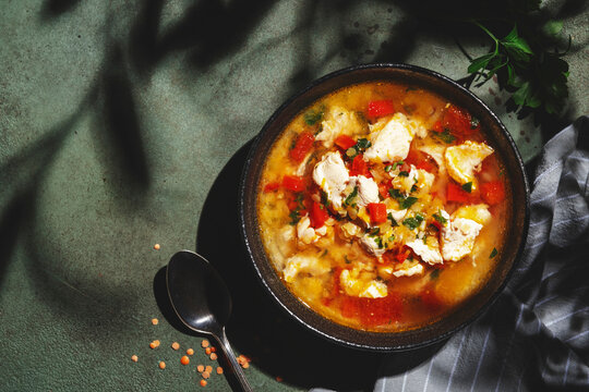 Warming autumn soup with red lentils, chicken fillet, vegetables, spices and paprika, comfort food. Green table, hard light with leaf shadows, top view