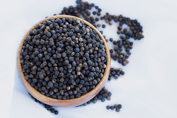 Fototapeta na wymiar A large number of black peppercorns placed in a wooden cup were placed on a white cloth.