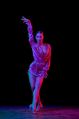Queen. Portrait of young graceful flexible woman dancing ballroom dance without partner isolated on dark background in neon light.