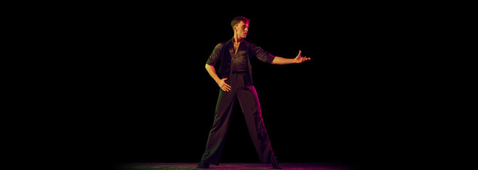 One young man, flexible male dancer in black costume standing alone isolated on dark background. Waiting for dance partner. Flyer for ad © master1305