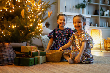 Two cute little girls under Christmas tree. Children under Christmas tree with gift boxes. New...