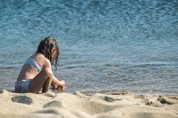 little girl in a swimsuit is on the seashore, playing with water and sand. Selective Focus girl