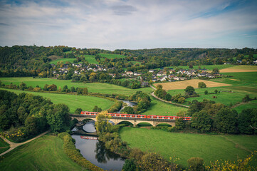 Blick in eine Landschaft mit Flusstal und Eisenbahnbrücke mit einem Zug darauf