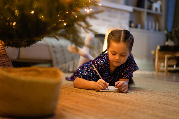 christmas, holidays and childhood concept - smiling girl making wish list or letter to santa at...