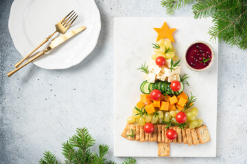 Christmas tree shaped Cheese Plate with crackers, grapes, cheese, tomatoes and cranberry sauce, winter holidays snack. Top view copy space