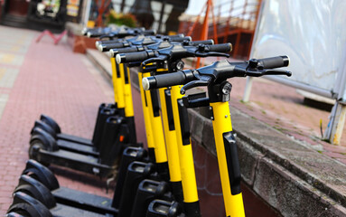 Parking of modern electric scooters on city streets.
Modern black and yellow electric scooters parked on the street of a modern city