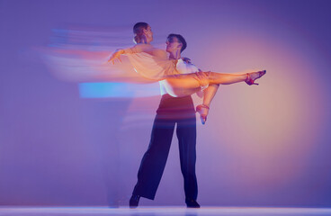 Art in motion. Flexible adorable ballroom dancers in stage attires dancing isolated on purple background in neon mixed light. Music, dance, emotions