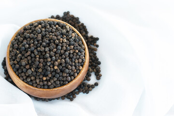 A large number of black peppercorns placed in a wooden cup were placed on a white cloth.
