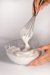 A whisk lifting glossy meringue, showcasing the perfect peak stage of whipped egg whites. The start...