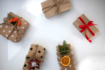A group of gifts in eco packaging, decorated with a dry orange, cinnamon stick, red ribbon and a fir branch. New Year's gift on white background, top view