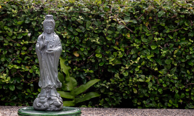 Figurine of Green Guan Yin Bodhisattva or Quan yin buddha statue (Goddess of mercy) with green leaves background. Space for text, Selective focus.