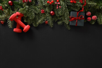 Christmas sport composition with gift and two red sports dumbbells on black background. Top view...