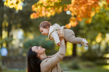 Beautiful young mother with a cute little girl 7 months old walks in the autumn park. Portrait of a happy family. Fall.