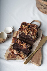 top view of a chocolate banana cake cut into slices on a wooden board. on the left side there is an egg shell. on the right side there is a cutting knife. white background.