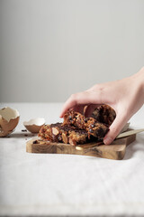 the hand is taking a piece of cake. the cake is on a wooden board. on the left there is a piece of eggshell. on the right there is a cutting knife. white background. negative space.