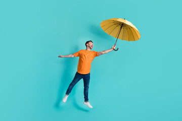 Full length photo of positive man stylish orange clothes yellow parasol flying empty space isolated on aquamarine color background © deagreez