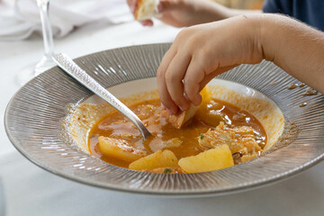 Children hand, dipping bread in a cod stew with potatoes and almonds that looks delicious