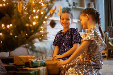 Two sisters playing near the Christmas tree and gifts. Happy little girls decorating christmas tree...