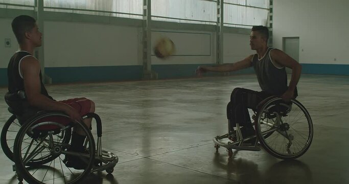 Two Brazilian hispanic paraplegic disabled athletes playing basketball outdoors passing ball to team member. Determination and sport with disability concept