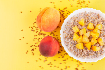 Fototapeta na wymiar Buckwheat porridge with milk and peach in a white bowl (plate) on an orange background. Space for text. Porridge for a child (baby). Healthy breakfast with fruit.