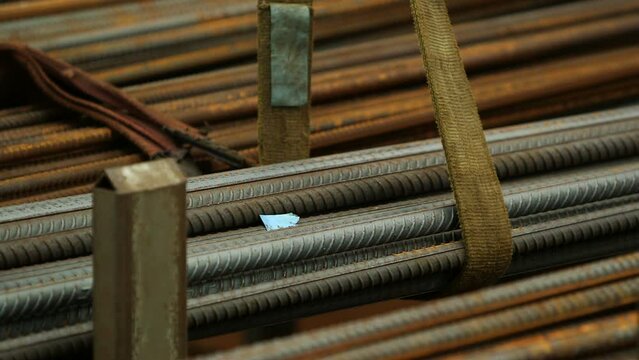 A stack of steel bars is being lowered down. A glimpse of a person passing by as the rope is released from it at a slow speed