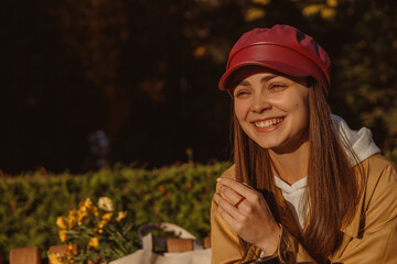 Joyful woman in cap and trench laughing and enjoying autumn in park in sunny sunset while looking away and having fun expressing happiness 