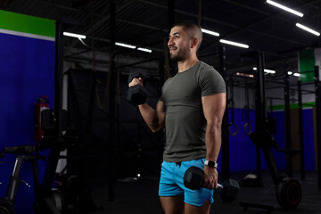 Fototapeta na wymiar vertical image of a latin athlete, doing bicep exercises with two dumbbells in a gym
