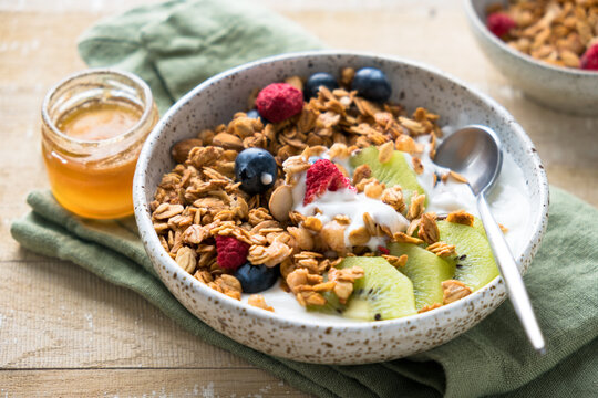 Oat honey granola bowl with fruits and yogurt on a wooden table background