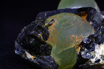 Chunk of real green prehnite spheres and dark green almost black epidote spikes on matrix macro isolated on black surface 