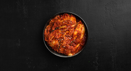 Kimchi in a black bowl on a black background, traditional Korean food, top view, copy space  - obrazy, fototapety, plakaty