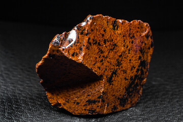 Real shiny specimen of orange Mahogany Obsidian volcanic stone macro isolated on black leather...
