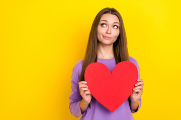 Photo of attractive cute girlish woman hold dreamy big red paper heart pouted lips smiling looking empty space minded date app isolated on yellow color background