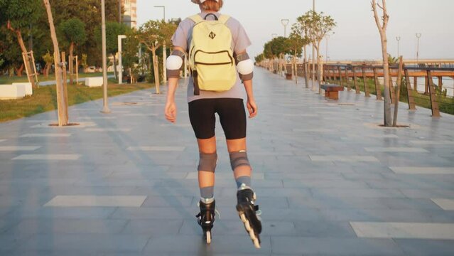 Following young sporty woman, rollerblading in the city with backpack.