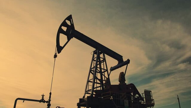 Low angle shot of working oil pump on oil field at sunset background. The industrial equipment. Oil industry, crude oil prices concept.