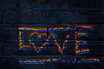 Hand draw with word LOVE, Colorful rainbow writing letter on old black brick block, Symbol of gay, Lesbian, Bisexual and transgender, LGBT social movements, Abstract geometric pattern background.