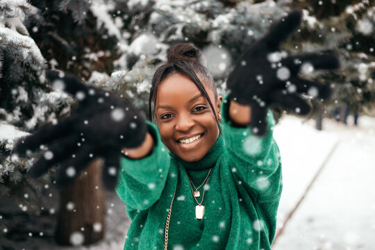 African american woman standing street outside near Christmas Tree, playing catches with hands up, white snow falling down. New Year atmosphere, winter vacation, cold weather

