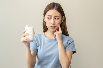 Allergy asian young woman, girl looking, holding glass of milk, face in thinking before drink milk as it may upset her stomach ache, pain. Lactose intolerance and dairy food , health problem concept.