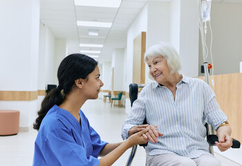 Psychological support from nurse to elderly woman sitting in wheelchair on corridor of medical clinic. Caring for people with disabilities at hospital