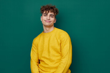 Obraz na płótnie Canvas a handsome man stands on a green background in a yellow sweater and smiling pleasantly poses relaxed looking at the camera. Horizontal photo with empty space