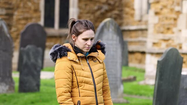 Young girl walking slowly and paying respects at a grave in church cemetery, close up