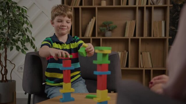 School kid building colour wooden blocks tower sitting at therapist office. Awareness of children's mental health. Over the shoulder view.