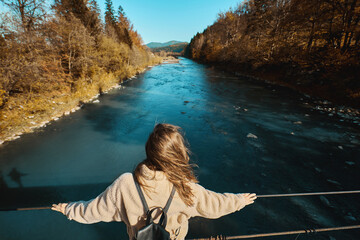 Back view of tourist woman with backpack enjoying nature scenic view on a suspended bridge over a mountain river. People in travel