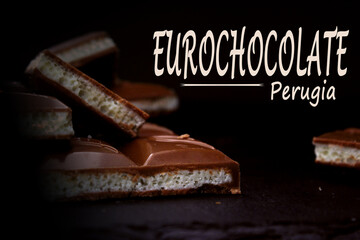 Pieces of milk aerated chocolate close-up on a dark background with an inscription. The concept of...