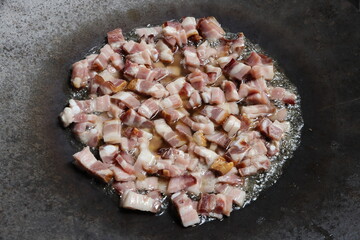 Sliced ​​raw bacon with a lot of fat, is fried in a large bowl. Illustration photo of uhealthy eating or not vegetarian lifestyle.