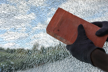Gloved hands with a brick are destroying a laminated security glass window, violence and vandalism concept, copy space