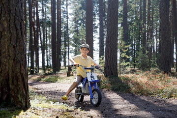Fototapeta na wymiar Satisfied little boy biker motorcyclist rides electric motorcycle through the forest