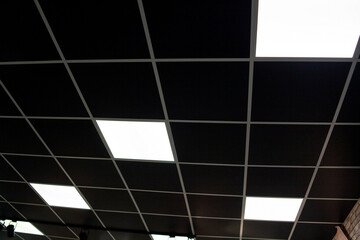 black ceiling with neon light bulbs in uprisen view. Fluorescent light in office interior with dark ceiling. - Powered by Adobe