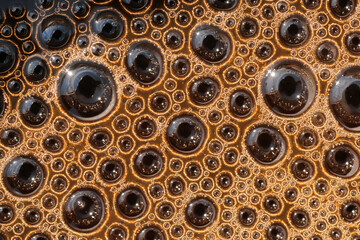 Close-up minimalistic, abstract photo of round bubbles of coffee's warm brown foam surface.
