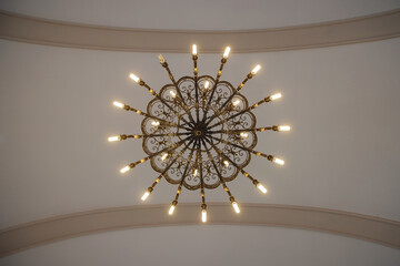 Old, elegant large chandelier hangs from the ceiling of the church dome, filled with energy saving compact fluorescent lights. Color interior architectural symmetrical style photo.