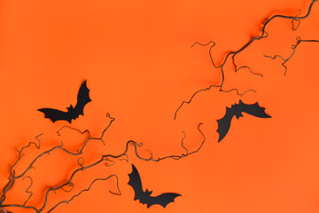 Three black paper bats, bare twigs on bright orange background. Festive spooky Halloween composition. Fall seasonal sale layout. Top view, flat lay. Copy space.